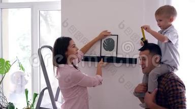 在公寓装修期间，一对年轻夫妇带着小男孩在墙上<strong>挂画</strong>